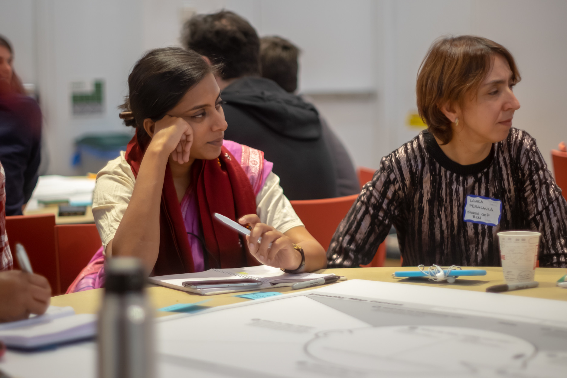 Salonie from SEWA and Laura from Suara Coop sitting in front of papers and pens, looking and listening to the speaker, who is sitting at the same table.